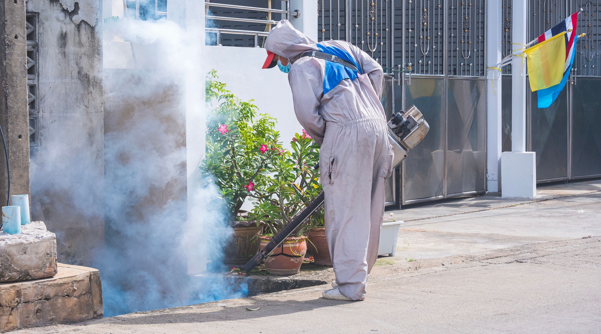 Healthcare worker spraying insecticide in drainage ditch on roadside area in residential district for eliminate mosquitoes
