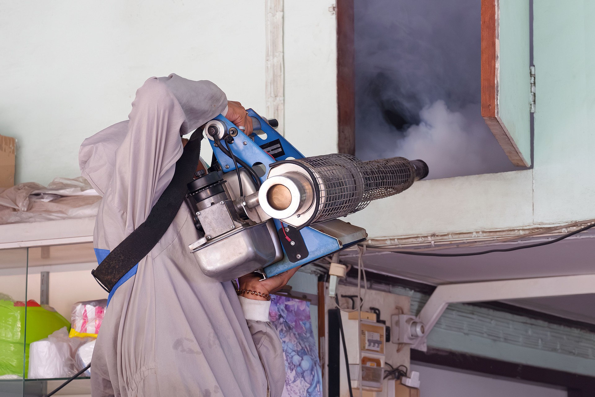Outdoors Healthcare worker in protective clothing is spraying chemical to eliminate mosquitoes into the door of attic room